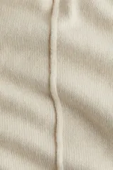 Buzo oversized de punto suave, color beige, con cuello alto acanalado y abertura posterior en V. Presenta hombros caídos, costuras decorativas verticales en el frente y terminaciones acanaladas en puños y bajo.