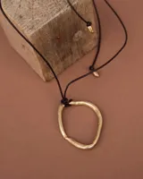 Collar con dije colgante de forma orgánica e irregular, acabado dorado, suspendido de un cordón negro de algodón natural.