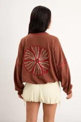 Campera oversize color crudo de algodón con spandex, corte de largo intermedio, mangas largas con detalles de costuras en zigzag bordadas y un gran diseño bordado a mano de una flor en la espalda.