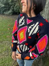 Sweater tejido a mano en lana con diseño geométrico multicolor en tonos naranja, rosa, verde y blanco sobre fondo azul marino. Diseño único e irrepetible.