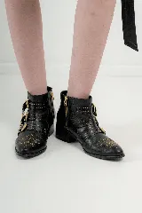 Botas cortas de cuero negro con tachas doradas, hebillas doradas y cierre lateral.