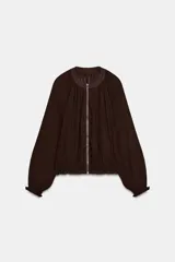 Chaqueta de organza plisada color marrón oscuro, con cuello redondo, cierre frontal con cremallera metálica, mangas largas con puños elásticos y bajo con acabado elástico.