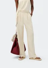 Pantalón de corte recto color beige con pinzas en la parte delantera y tira ajustable a modo de cinturón con nudos decorativos.