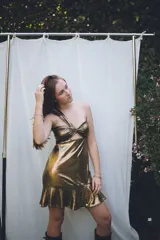 Vestido corto dorado metálico con escote asimétrico anudado al frente y un corte cut-out en el torso. La falda tiene un ruedo con volado.