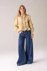 Camisa negra de corte entallado con volados decorativos en el cuello, la botonadura frontal, los hombros y las mangas. Presenta mangas largas con puños ajustados y un ruedo con volado inferior.