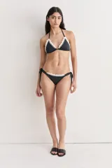 Bikini de dos piezas color negro con corpiño triangular y bombacha regulable lateralmente. Ambos bordes están decorados con puntilla de algodón tejida en crochet de color blanco.