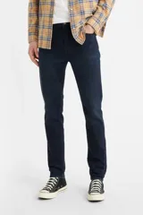 Jean de corte skinny y tiro medio, en color azul oscuro con acabado uniforme. Presenta costuras reforzadas y cierre frontal con botón y cremallera.