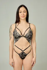Conjunto de lencería compuesto por un bralette triangular y una tanga, confeccionados en encaje negro con detalles florales en color hueso. El bralette presenta breteles ajustables y diseño con tiras decorativas, mientras que la tanga cuenta con doble tira lateral regulable.