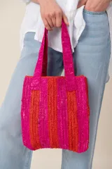 Bolso tipo shopper confeccionado en material texturizado, con diseño a rayas verticales en tonos fucsia y rojo, y doble asa de hombro.