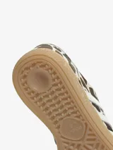 Championes Adidas modelo Handball Spezial W, con estampado animal print tipo vaca en tonos marrones y blancos, tiras laterales blancas, cordones celestes y suela de goma translúcida.