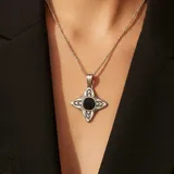 Dije con forma de cruz estilizada, elaborado en plata 925 y detalles en oro, con una piedra ónix negra circular engastada en el centro. Presenta un acabado texturizado y oxidado que resalta los detalles del diseño.