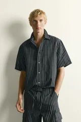 Camisa de corte relajado confeccionada en denim de algodón y lino, con diseño de rayas verticales, cuello solapa y manga corta con cierre frontal de botones.