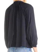 Blusa de gasa con plisado soleil, cuello a la base fruncido con escote en V regulable mediante lazos, y mangas largas abullonadas con puños sastreros.