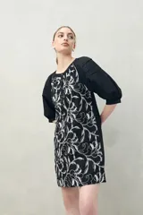 Vestido corto negro con bordado floral blanco, escote redondo con abotonadura frontal y mangas 3/4 abullonadas con pliegues en los hombros.