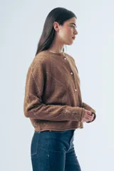 Cardigan de punto color marrón con diseño de rombos bordados en hilo claro. Presenta cuello redondo, cierre frontal con botones y mangas largas con detalle de letras bordadas.