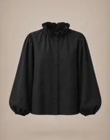 Camisa de lino color marrón chocolate, con cuello redondo adornado con volados, cierre frontal de botones y mangas largas abullonadas con puños ajustados.