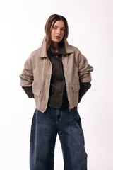 Campera corta de color beige con cuello alto estructurado, cierre frontal y bolsillos delanteros con solapa. Presenta un diseño minimalista de corte recto y mangas largas con puños acanalados.