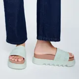 Sandalias plataforma Melissa modelo Cozy Slide M-Lover, color verde menta con plantilla marrón. Cuenta con una faja ancha superior con el nombre de la marca en relieve y suela chunky con relieve ondulado.