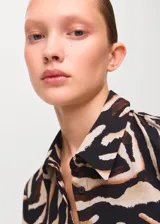 Camisa de poliéster con estampado de animal print estilo cebra en tonos negro, beige y marrón, de manga larga y cuello clásico con cierre frontal de botones.