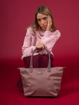 Bolso tipo shopper de nylon color rosa pálido/malva, con asas y detalles en cuero sintético marrón grisáceo. Presenta un parche con el logo de la marca en el frente.