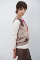 Chaleco de punto con diseño de rombos en tonos beige, marrón y gris. Presenta cuello redondo y corte ajustado a la cintura.