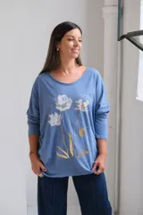 Remera de algodón color celeste, con cuello redondo amplio, mangas largas y estampa frontal de flores en tonos blanco y dorado.