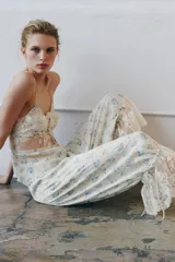 Pantalón bombacho de tiro medio y cintura elástica, confeccionado en viscosa con estampado floral y rayas sutiles. Presenta bajo ajustable con lazada y aplicación de encaje contrastante en el ruedo.