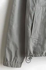 Campera rompevientos de nylon color gris, repelente al agua, con cuello elevado, cierre frontal y bolsillos laterales con botón a presión oculto.