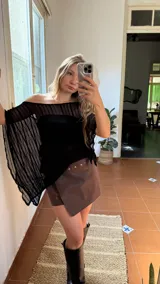 Pollera short de ecocuero color marrón, con diseño cruzado y detalle de tachas metálicas en la parte frontal. Cuenta con cierre ajustable mediante botones.