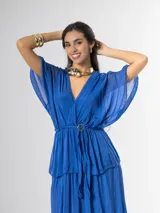 Vestido midi de seda italiana color azul, con escote en V, mangas murciélago amplias, falda de tres volados y cintura elastizada con lazo ajustable al tono y hebilla circular dorada.