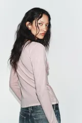 Chaqueta de punto color beige con escote en pico y manga larga, que incluye un top interior integrado con detalle de encaje a tono. Cierre frontal mediante botones.