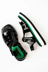 Sandalias negras con tiras anchas, plataforma blanca y detalles en verde.