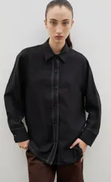 Camisa de corte holgado y diseño clásico, confeccionada en tela satinada con un sutil estampado floral tono sobre tono. Presenta cuello camisero, cierre frontal con botones y mangas largas con puños rectos.