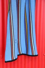 Vestido corto blanco con rayas verticales en azul, amarillo y marrón. Tiene escote redondo, breteles anchos y corte holgado.