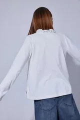 Blusa de estilo romántico con frente de lino y espalda y mangas de algodón con elastano. Presenta un diseño con mini volados en la pechera, cuello redondo y cierre frontal con botones.