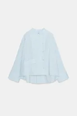 Camisa de corte oversize con estampado de rayas verticales, cuello redondo tipo mao y cierre frontal con botones. Presenta manga larga con puños anchos, un bolsillo de plastrón con solapa en el frente y bajo asimétrico.