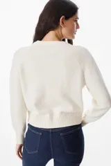 Saco tipo cardigan de punto color crudo, con cuello redondo, cierre frontal de botones y mangas largas con puños acanalados.