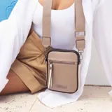 Phone bag color marrón claro con laterales beige, bolsillo frontal con cierre y tirador con flecos. Tiene espacio para celular y billetera, y correa de galón regulable y desmontable.