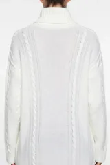 Polerón largo de tejido de punto en color blanco, con cuello alto y diseño de trenzas verticales. Presenta un corte amplio y mangas largas con puños acanalados.