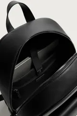 Mochila de diseño minimalista en color negro con acabado texturizado. Cuenta con un compartimento principal con cierre de cremallera, un bolsillo frontal con solapa y compartimento interior para dispositivos electrónicos. Incluye espalda acolchada, banda de sujeción para equipaje, asa de mano y correas de hombro ajustables.
