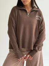 Sweater de tejido bremer color blanco, con cuello polo, cierre frontal y bordado en el pecho. Presenta mangas largas y diseño de corte holgado con terminaciones acanaladas.