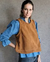 Chaleco de tela bucle color tostado, con diseño sin mangas, cuello redondo y corte recto. Presenta costuras verticales decorativas en el frente.
