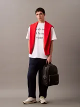 Mochila negra de cuero sintético con asa de mano y tirantes ajustables. Tiene un bolsillo frontal con cierre y el logo de Calvin Klein Jeans estampado en la parte inferior.