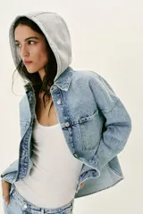 Cazadora de denim oversize con capucha gris desmontable, cuello camisero, cierre frontal con botones metálicos y bolsillos delanteros de plastrón.