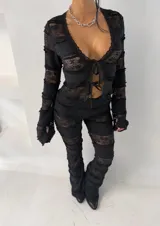 Conjunto de dos piezas compuesto por top de manga larga con cierre frontal de lazos y pantalón de corte acampanado. Ambas prendas están confeccionadas en encaje negro con diseño de franjas horizontales superpuestas.