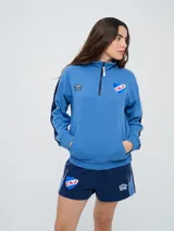 Buzo de felpa azul marino con medio cierre, cuello alto, bandas laterales en tono rosado y bolsillo frontal tipo canguro. Presenta el logo de Umbro y el escudo del Club Nacional de Football bordados.
