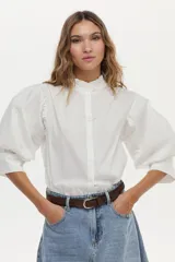 Camisa blanca de cuello mao con volados, mangas abullonadas y cierre frontal con botones.