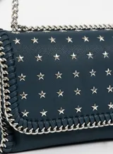 Cartera de hombro color azul marino, con solapa frontal decorada con tachas en forma de estrellas plateadas. Los bordes están adornados con un detalle de cadena entrelazada y la correa es una combinación de cadena plateada y una sección de cuero sintético.