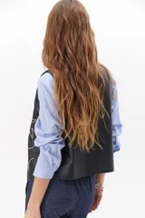 Chaleco marrón de simil cuero con bordado en color crema, cuello en V y cierre frontal con botones.