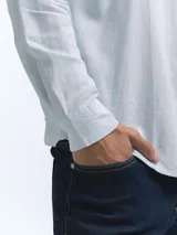 Camisa de manga larga, color blanco, con cuello camisero y botones frontales. El tejido presenta una textura visible de lino.